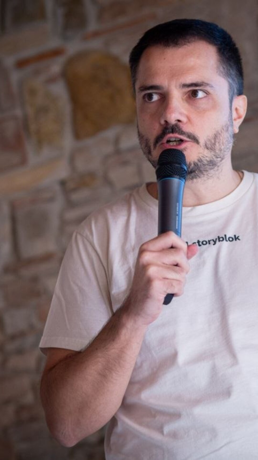On stage at Come To Code, speaking into a microphone against a stone wall.