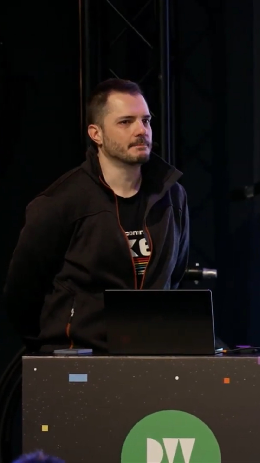 On stage at Devworld behind a branded podium in a dark jacket.