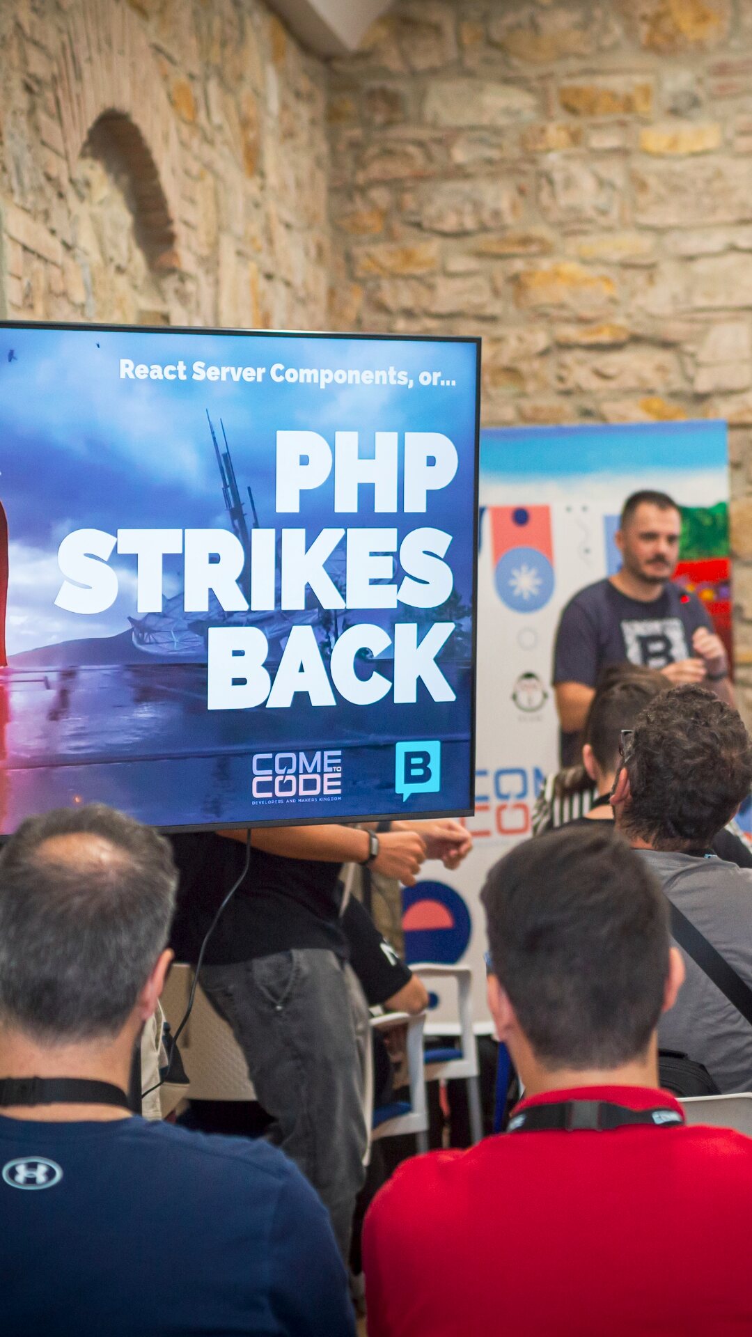 Standing beside a screen reading “PHP Strikes Back” in front of a seated audience.