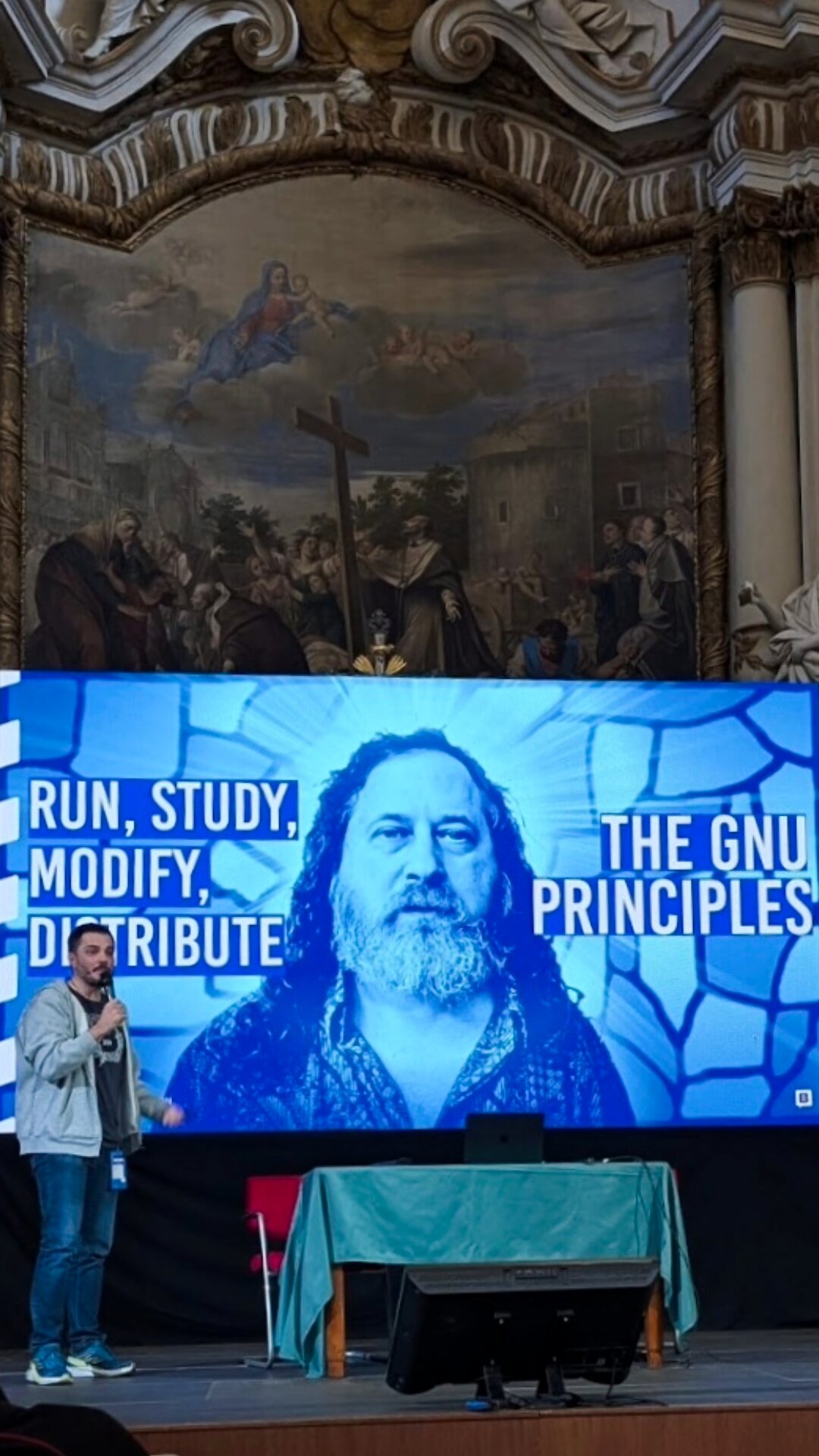 Speaking in a baroque hall beside a slide about the GNU principles.